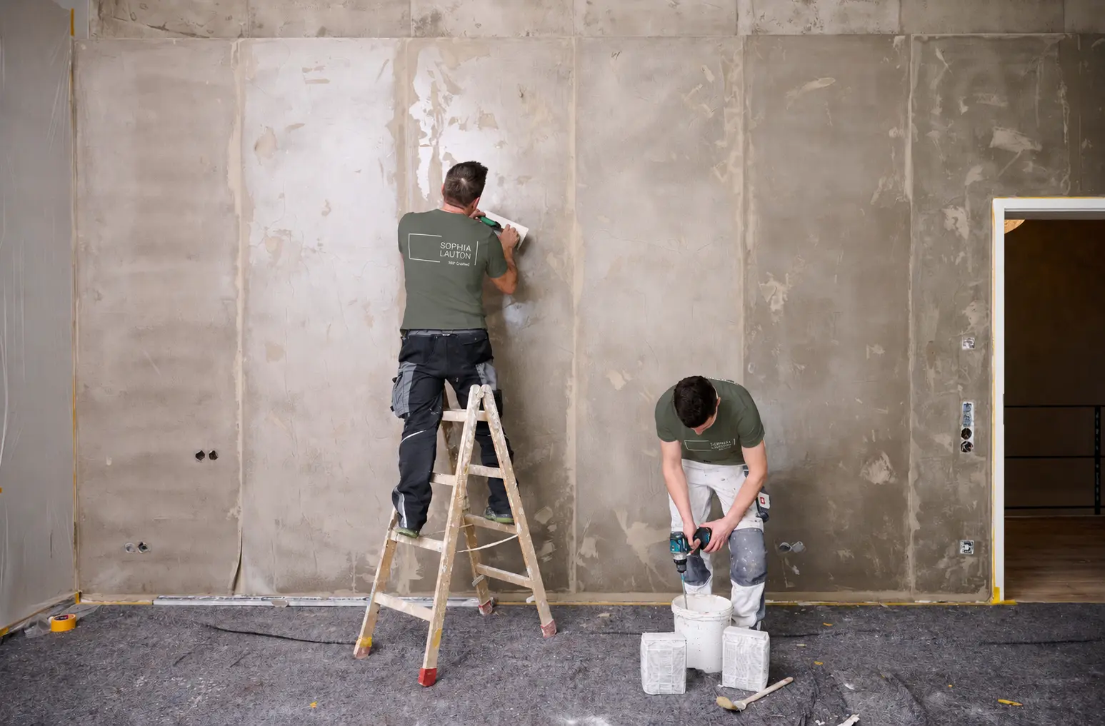 Zwei Handwerker beim Spachteln und Anmischen vor einer vorbereiteten Innenwand