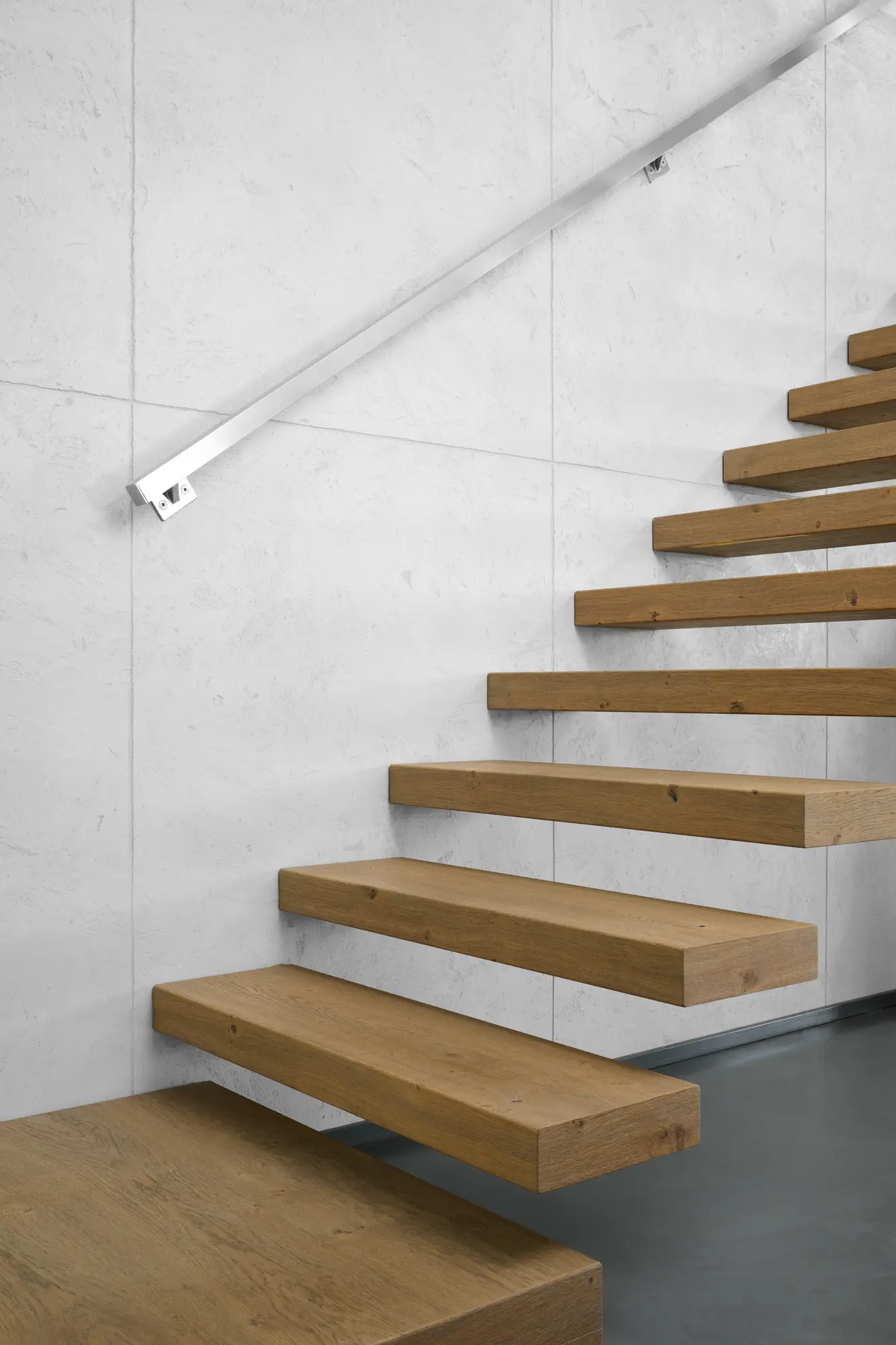 Freitragende Holztreppe vor Sichtbetonoptik und grauem Boden