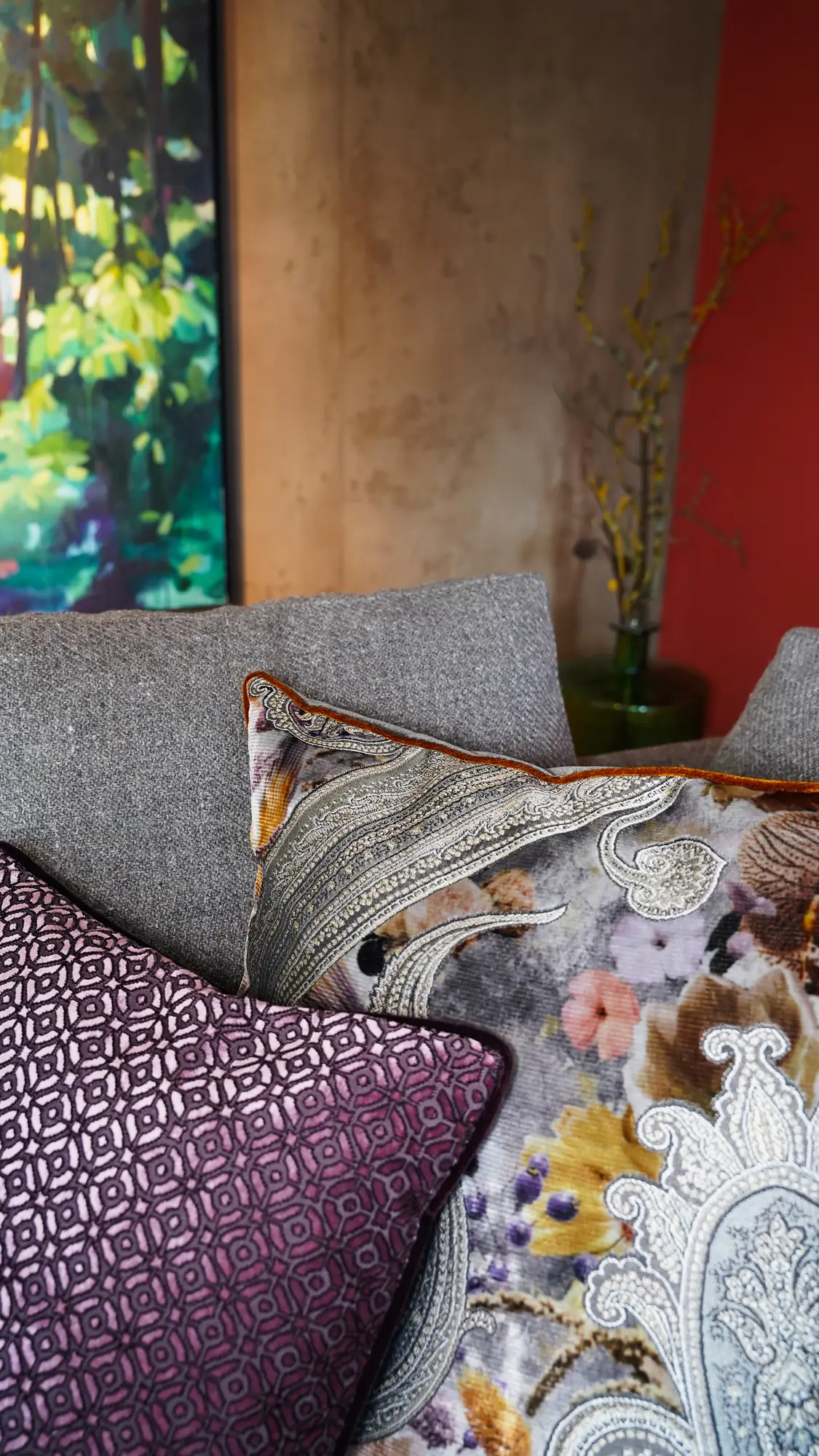 Graues Sofa mit gemusterten Kissen vor farbigen Wänden