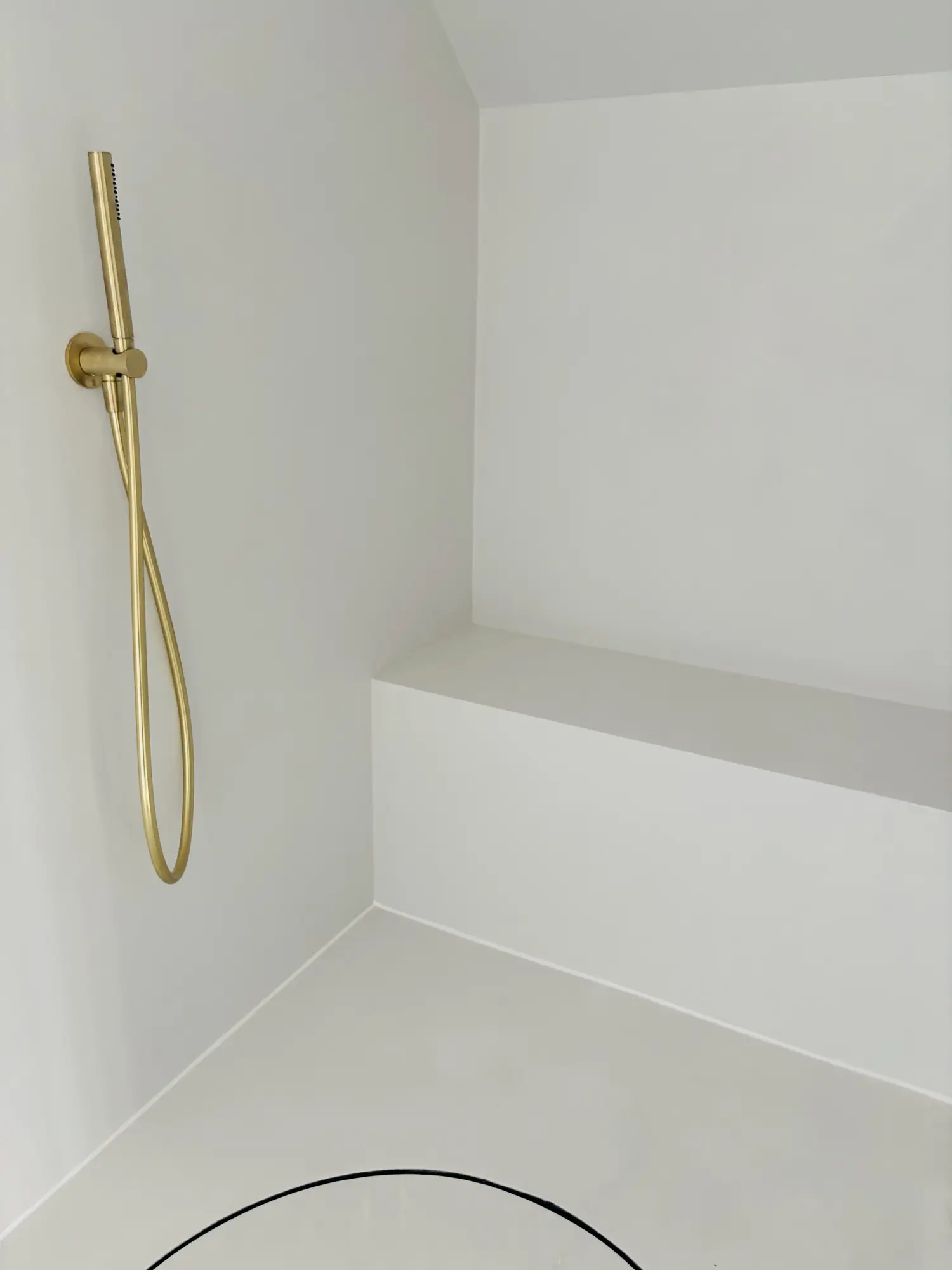 Minimalistische weiße Dusche mit Sitzbank und goldfarbener Handbrause